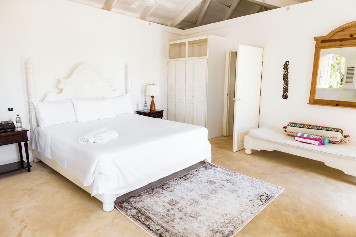A bedroom with a large bed, a bedside table with a lamp, a small bench with books, and a wardrobe.
