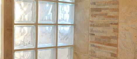 Un baño con cabina de ducha de vidrio, un cabezal de ducha y pared de azulejos.