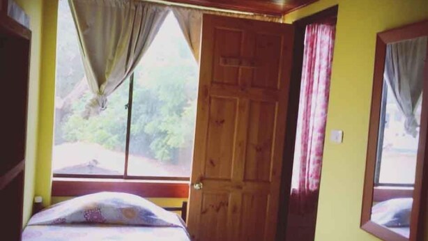 A room with a bed, a wooden door, and a window with curtains.
