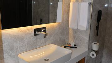 A modern bathroom with a large mirror, a white sink, a shower, and a toilet.