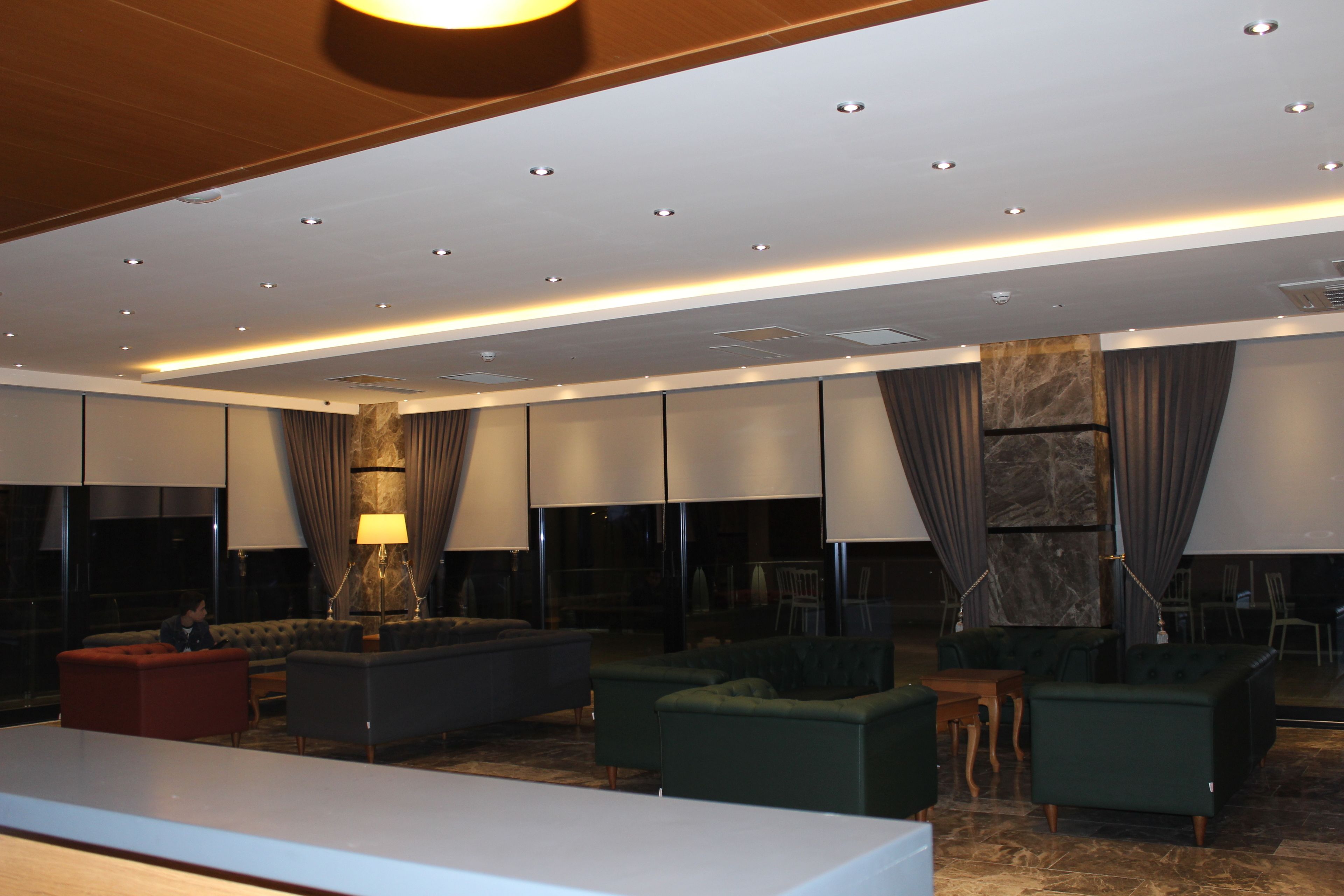 Un hall d’hôtel moderne doté d’un long comptoir d’accueil, de plusieurs espaces de détente et d’un grand mur agrémenté d’un élément décoratif en pierre.