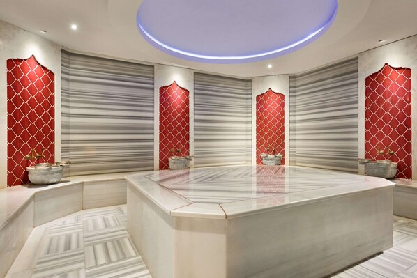 Un baño moderno con un amplio tocador de mármol, paredes de diseño rojo y un accesorio de luz circular.