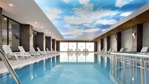 Piscina interior moderna con sillones de descanso y un techo con diseño de nubes.