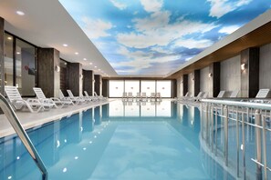 A modern indoor swimming pool with lounge chairs and a ceiling with a cloud design. - Ramada by Wyndham Giresun Piraziz (Piraziz)