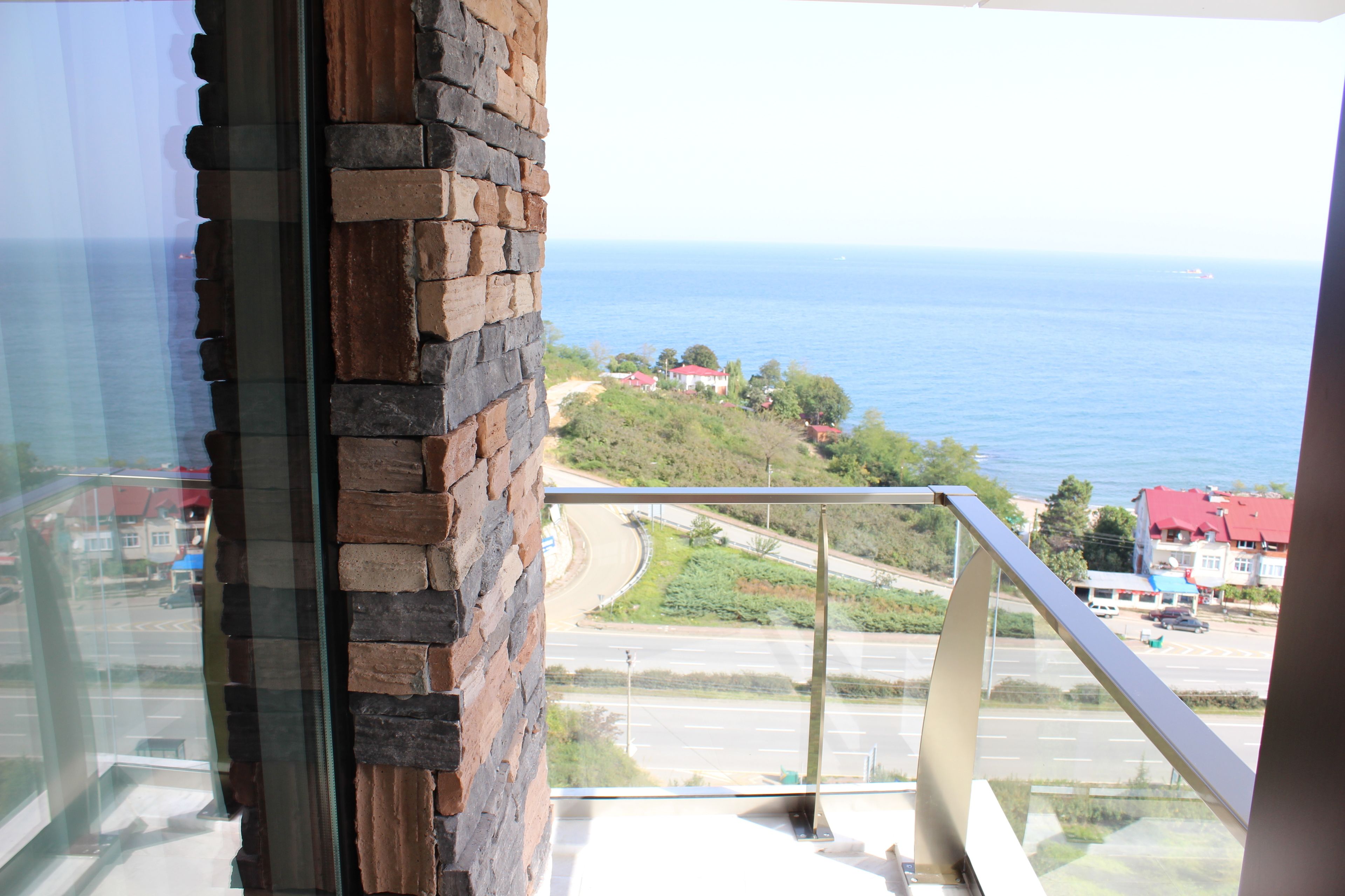 A view from a balcony overlooking a coastal road with a clear blue sea in the background.