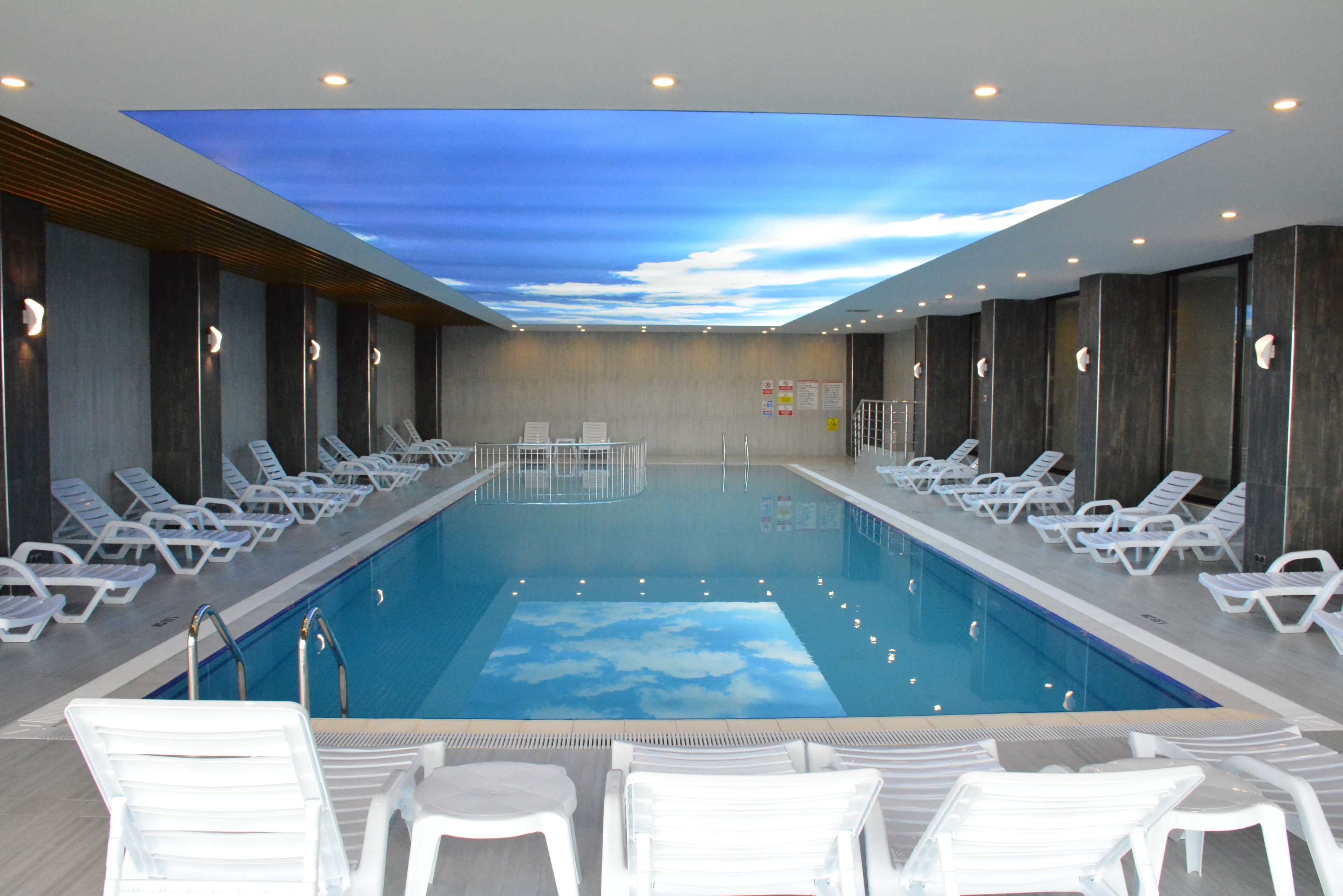Una piscina con techo de cielo, rodeada de sillones blancos y una zona de solarium.
