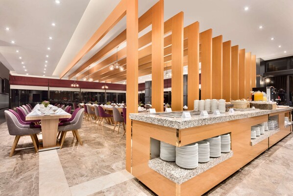 Un comedor moderno con una larga mesa y sillas, un mostrador tipo buffet con platos y cestas, e iluminación empotrada en el techo.