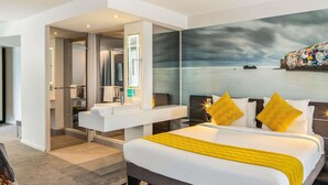 Una habitación de hotel moderna con una cama grande, un baño con tocador y vistas al mar.