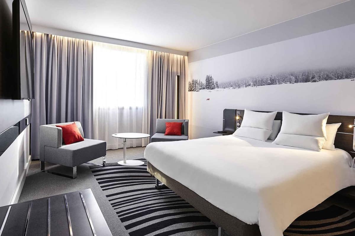 Una habitación de hotel moderna con una cama grande, un sofá, una mesita y un televisor.