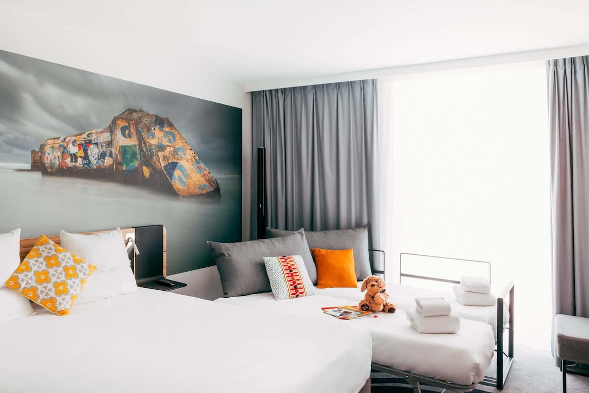 Habitación de hotel con dos camas, un cuadro grande en la pared y vistas al mar.