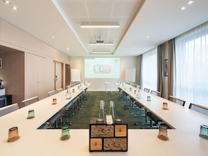 Un salón de conferencias con una larga mesa, sillas, una pantalla de proyector y una presentación.