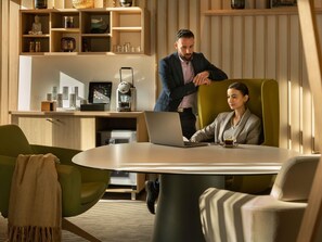 Un espacio de oficina moderno con una mesa redonda, dos sillas, una máquina de café y un estante con diversos objetos.