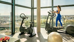 Un gimnasio con equipo de ejercicios y un amplio ventanal que ofrece vistas al aeropuerto.