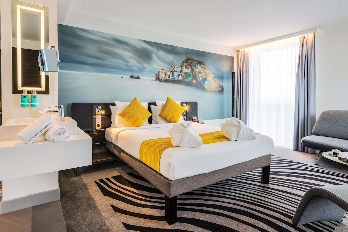 Una habitación de hotel moderna con una cama grande, una zona de estar, un baño y vistas al mar.