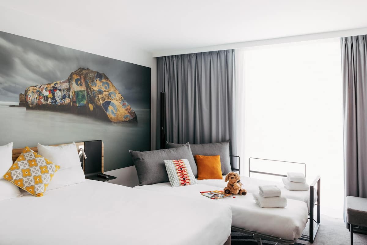 A hotel room with two beds, a large abstract painting, and a view of the sea.