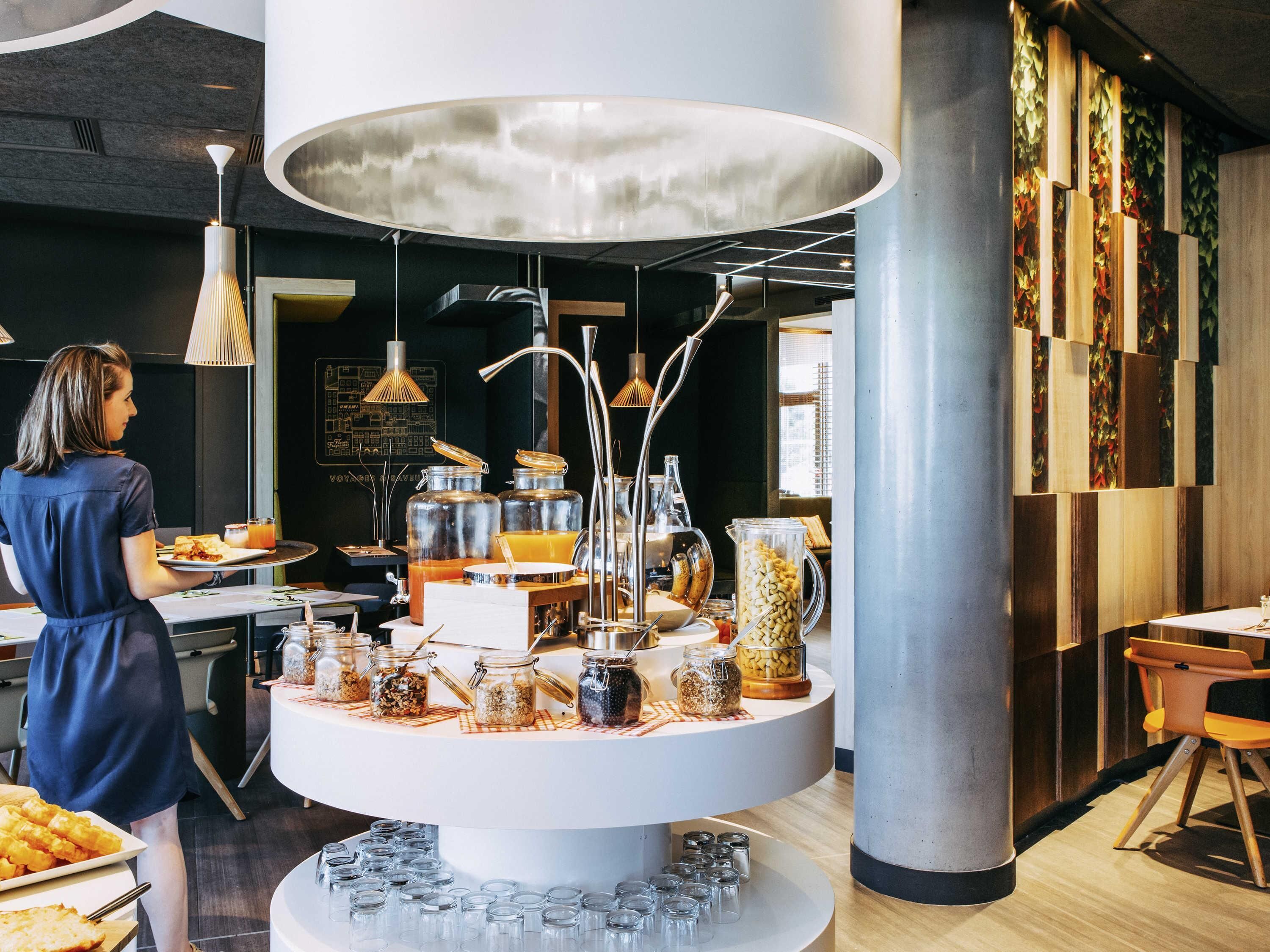 A breakfast buffet with various food items and beverages, a central decorative light fixture, and a modern interior design.