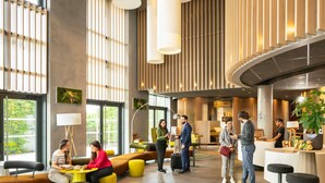 Un moderno vestíbulo de hotel con techos altos, ventanas amplias y una escalera central.