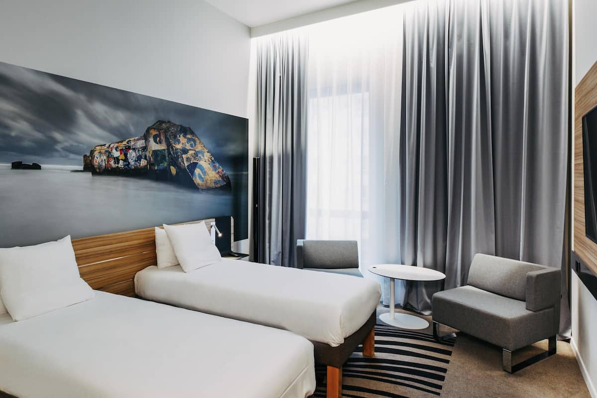 Habitación de hotel con dos camas, un sofá, una mesita redonda y un cuadro en la pared.