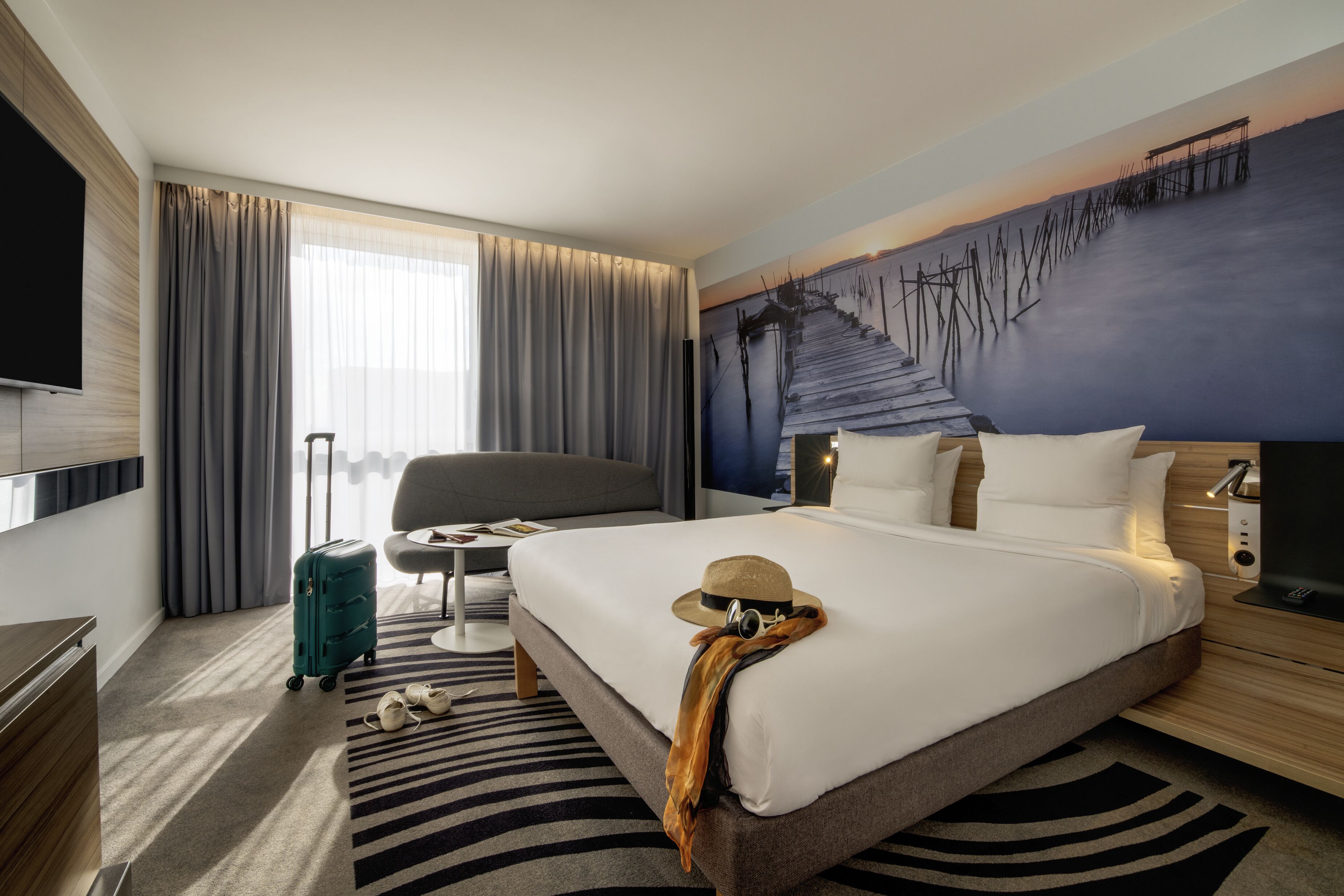 Een hotelkamer met een groot bed, een televisie, een bureau en een raam met gordijnen.