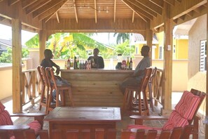 A wooden bar area with a counter, bar stools, and a seating area with striped cushions.