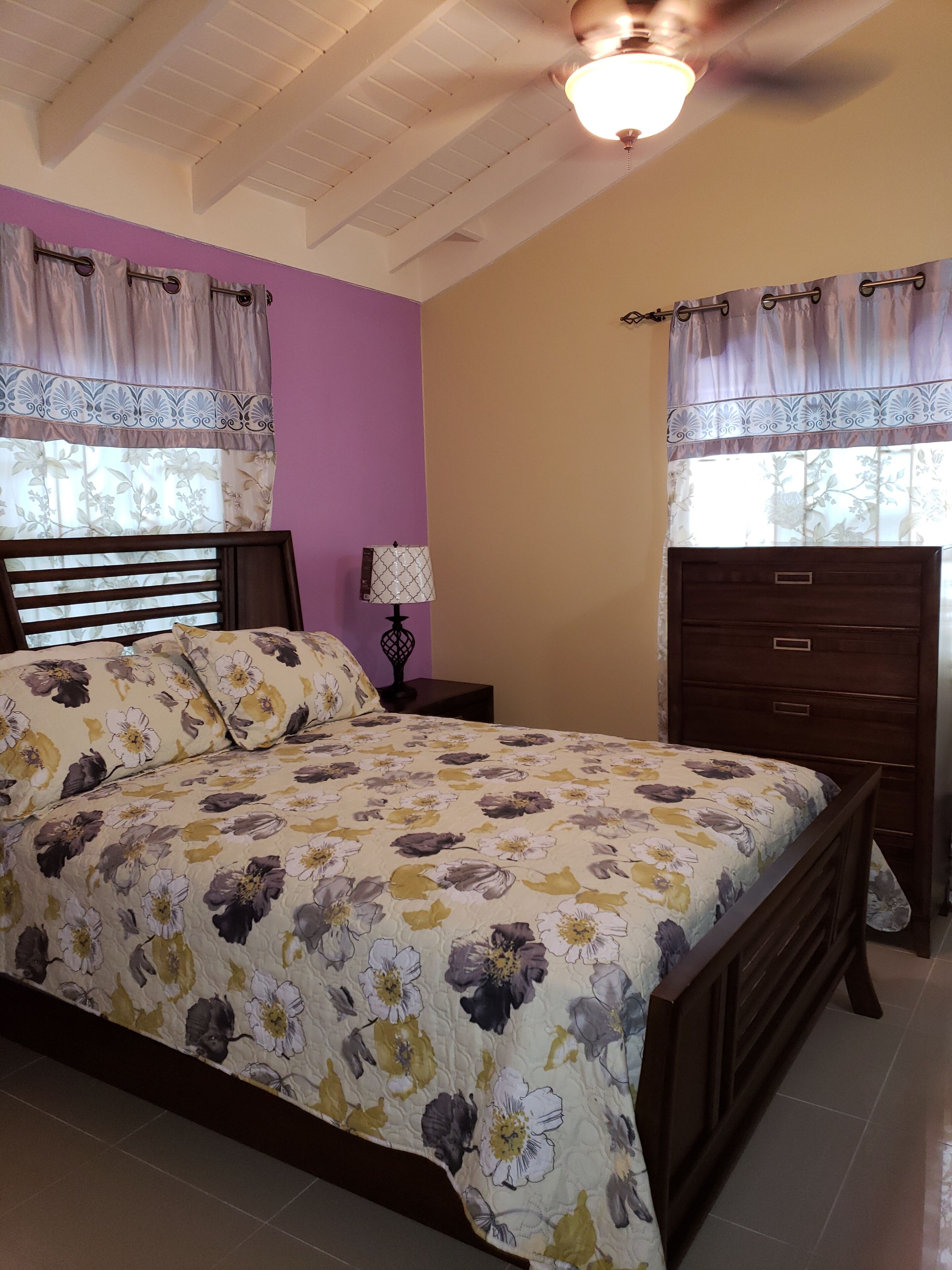 Une chambre à coucher comprenant un lit, une table de chevet, une commode et un ventilateur de plafond.