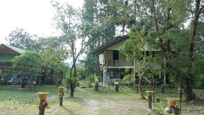Um edifício rústico com telhado inclinado, rodeado por vegetação exuberante e árvores.
