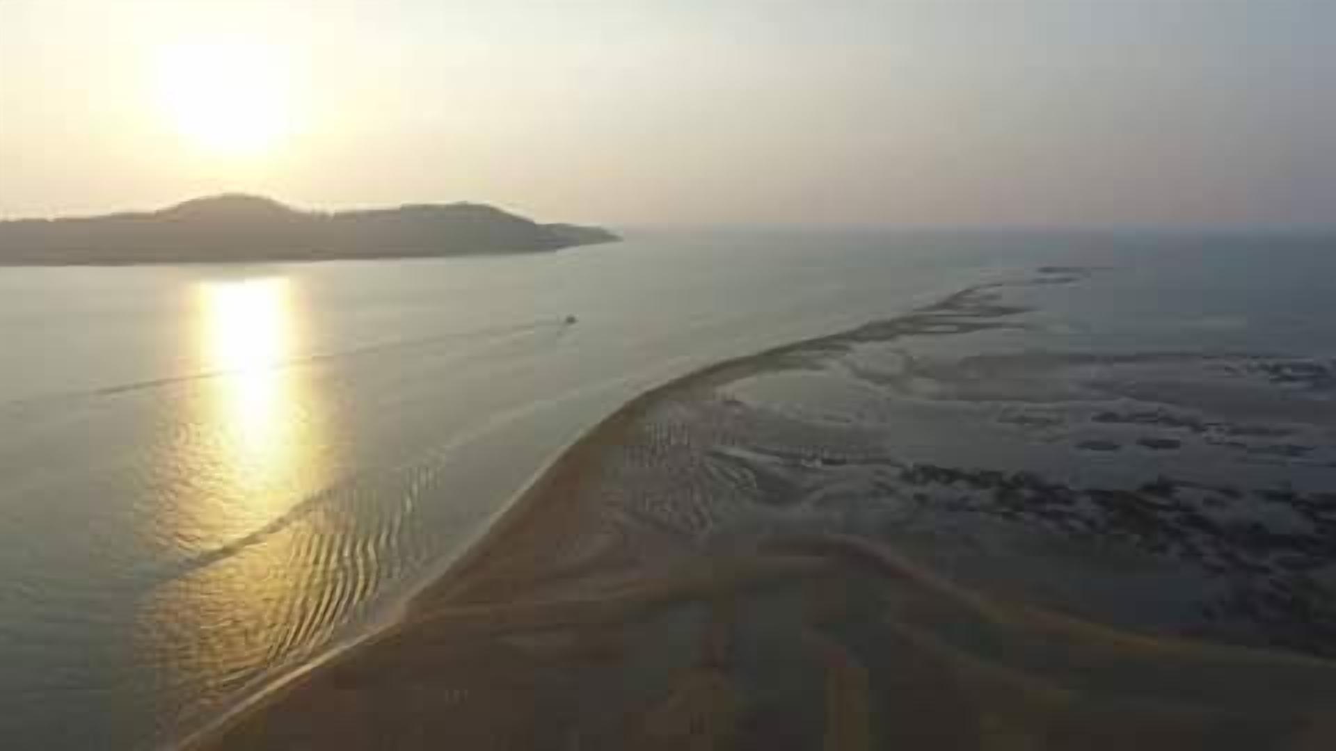 A coastal landscape with a sandy beach and calm waters.