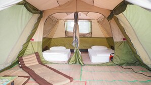 Uma tenda com duas camas, uma janela central e um tapete no chão.