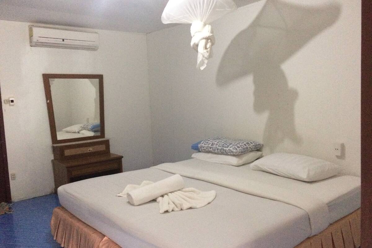Quarto com cama, espelho, mesa de cabeceira e luminária suspensa.