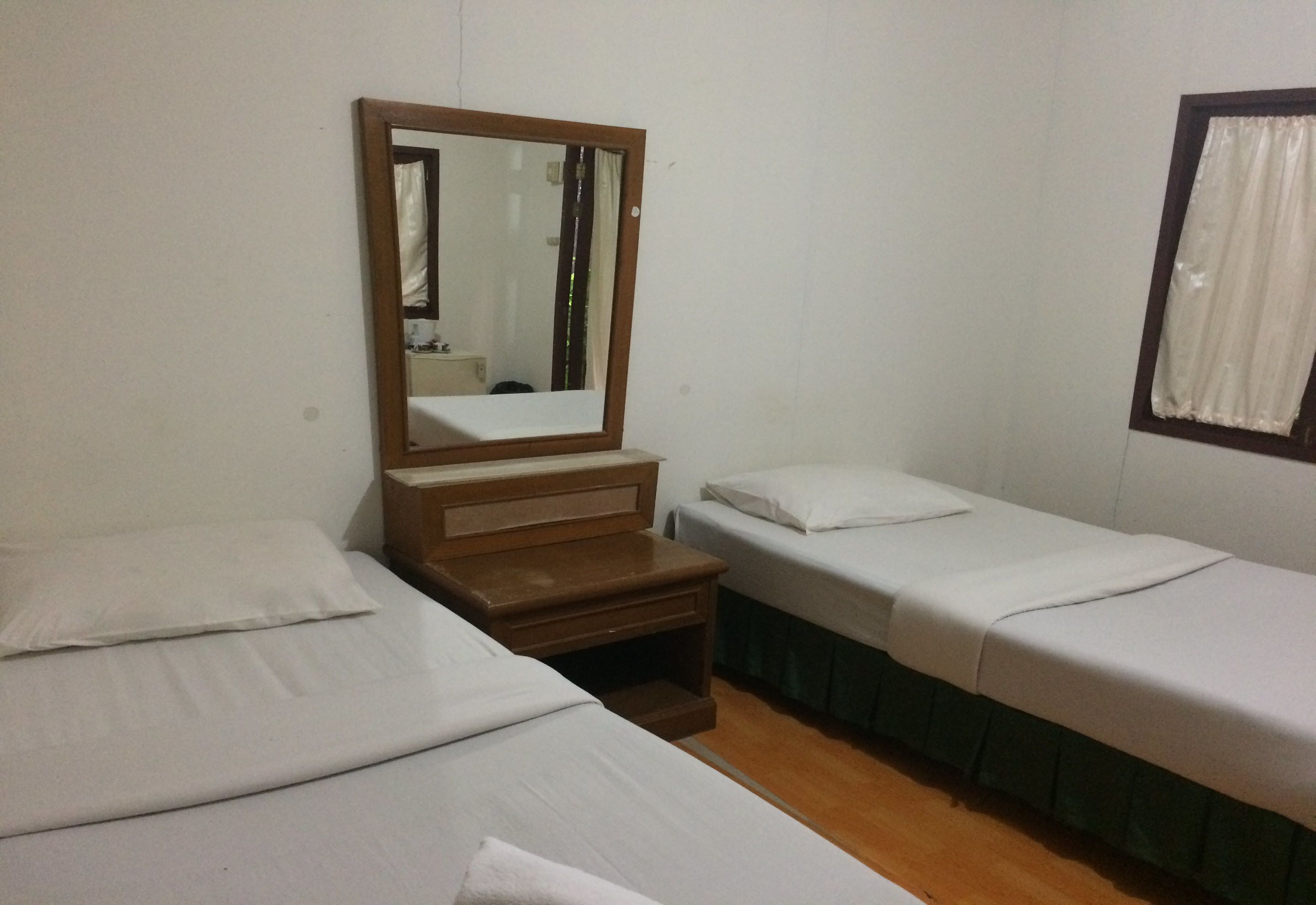 Una habitación con dos camas individuales, una mesita de noche de madera, un espejo y una ventana con cortinas.