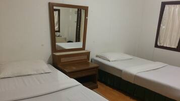 Una habitación con dos camas individuales, una mesita de noche de madera, un espejo y una ventana con cortinas.