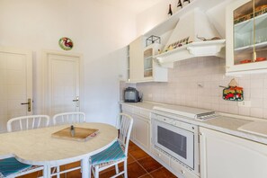 Una cocina compacta con muebles blancos, una mesa de comedor con sillas, un microondas y un horno pequeño.