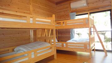 A cabin with three bunk beds, wooden walls, and a window with a view of trees.