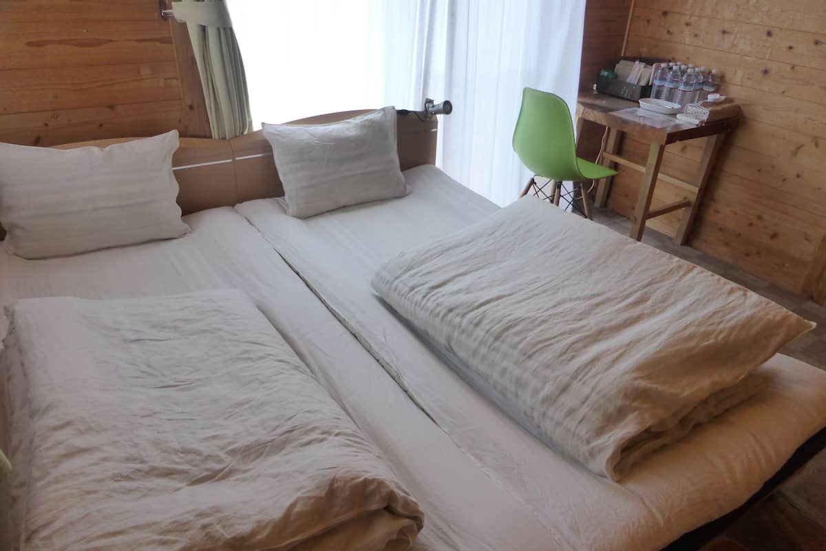 A double bed with white linens, a wooden headboard, a green chair, and a small table with toiletries.