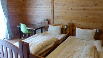 A wooden cabin room with two beds, a desk, and a green chair.