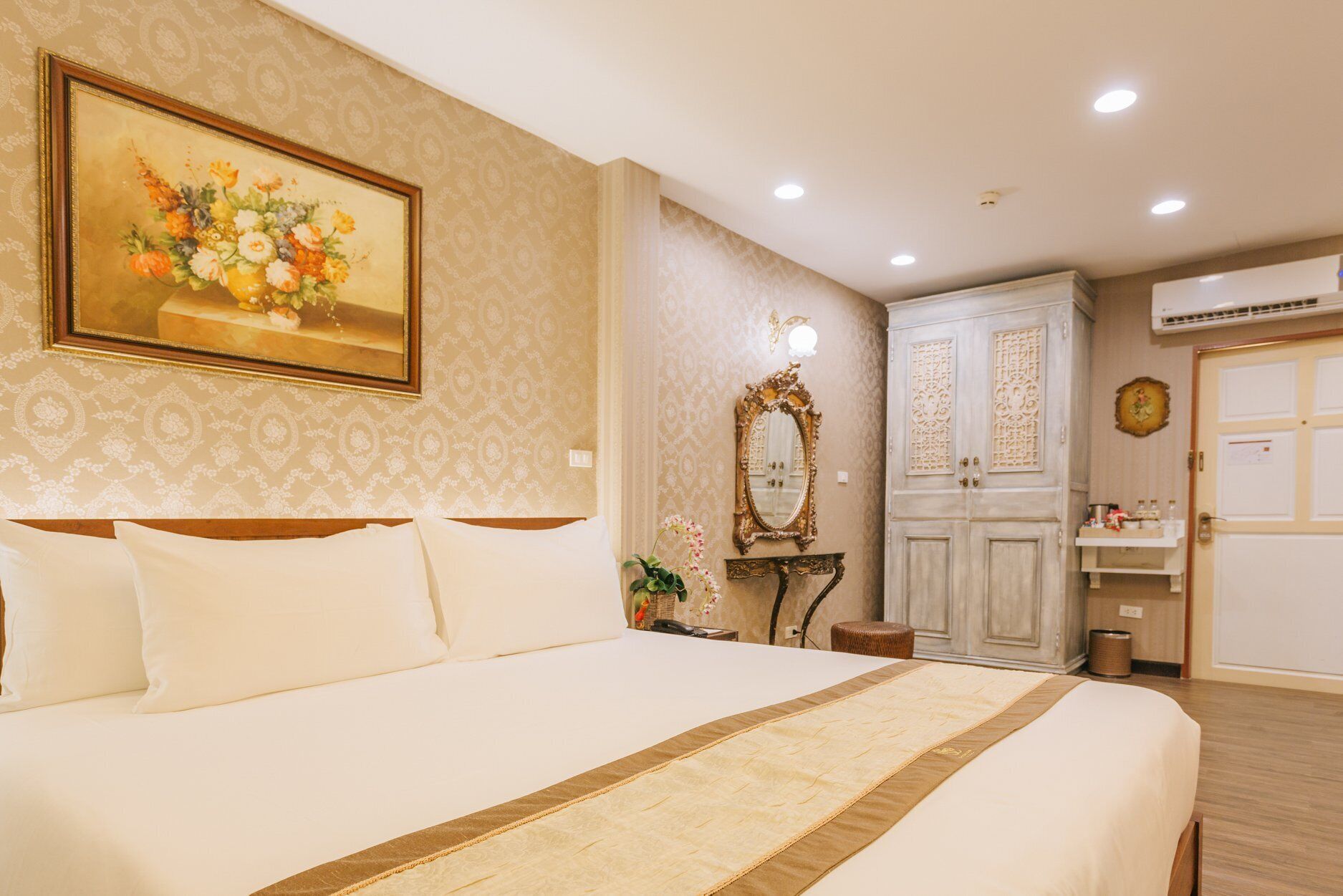 A hotel room with a large bed, a vanity with a mirror, and a wardrobe.