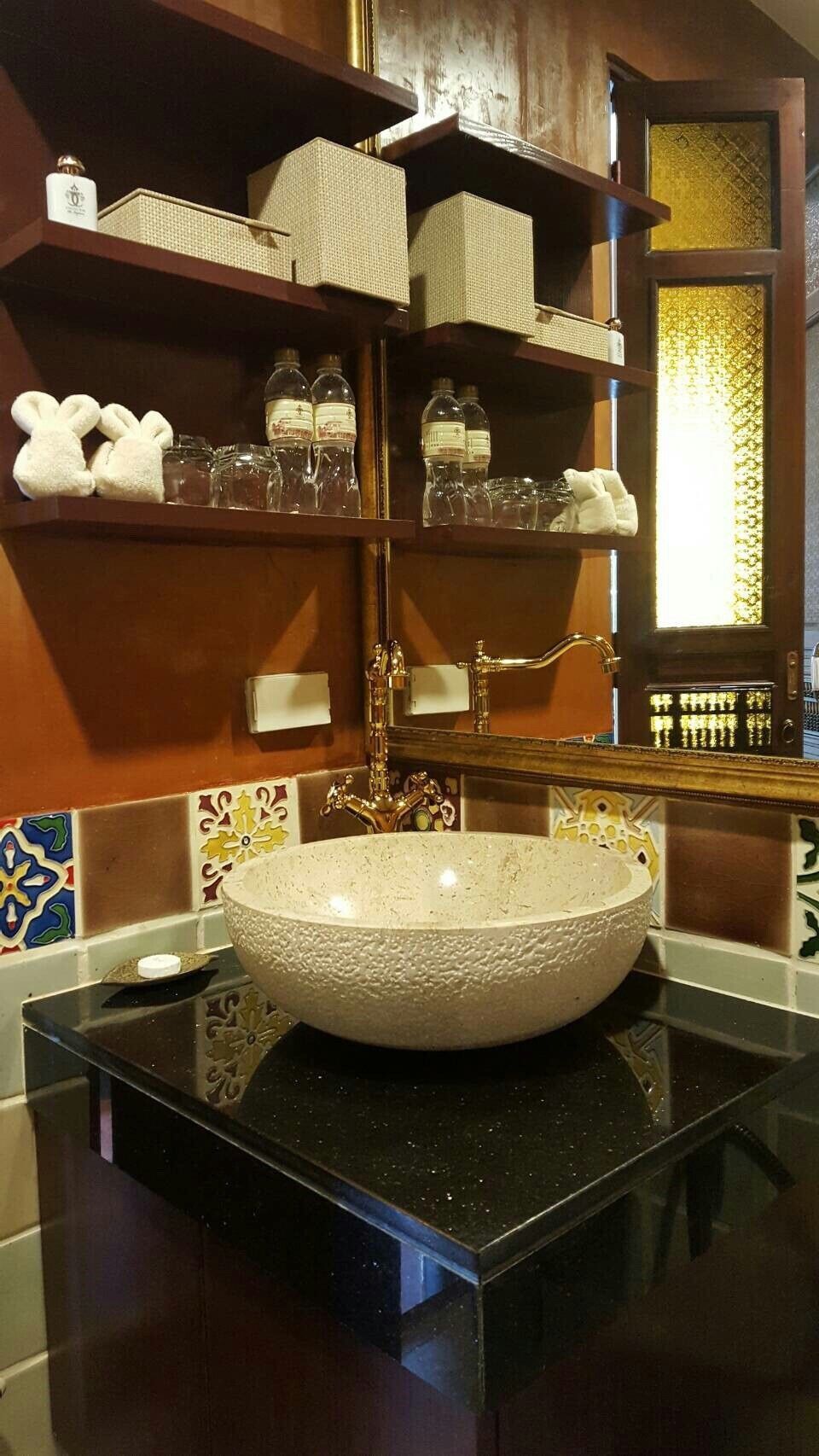 Un baño con un lavabo grande de diseño, estantes con artículos de tocador y un espejo decorativo.