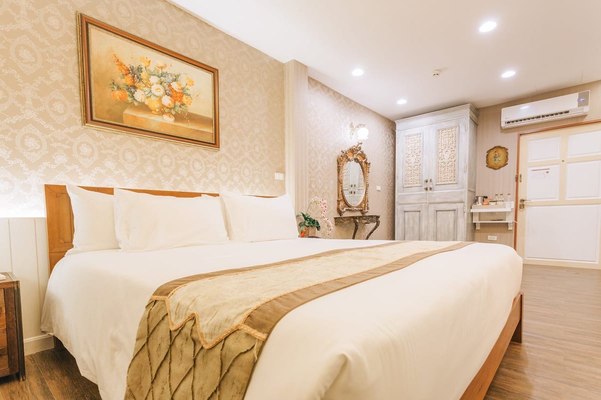 A well-lit bedroom with a large bed, a vanity with a mirror, and a wall-mounted air conditioner.