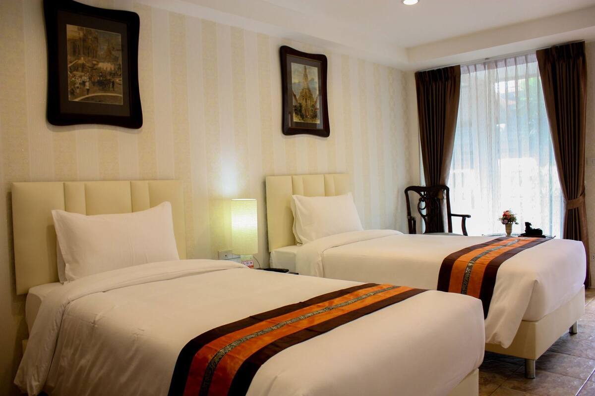 A hotel room with two beds, a nightstand, a lamp, a chair, and a window with curtains.