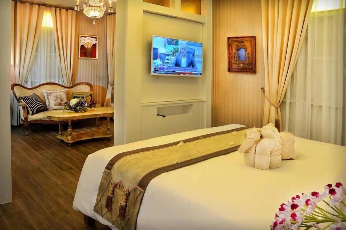 A hotel room with a bed, a sofa, a TV, and a wall-mounted TV.