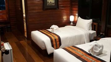 A hotel room with two beds, wooden paneling, an air conditioning unit, a framed picture on the wall, and a bedside lamp.