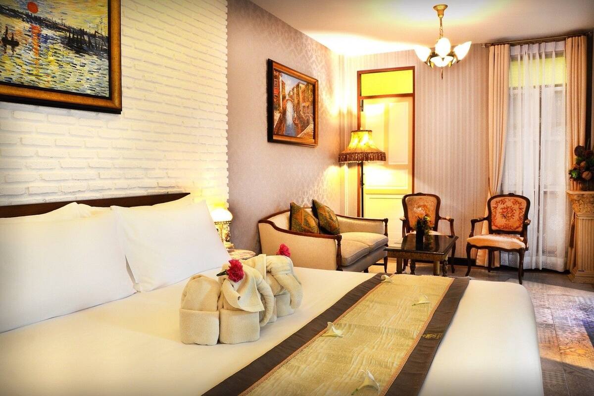 A hotel room with a large bed, a sofa, two armchairs, a table, and a painting on the wall.