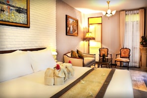Quarto de hotel com uma cama grande, um sofá, duas poltronas, uma mesa e um quadro na parede.