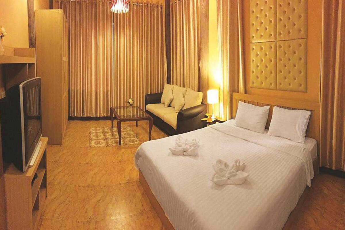 A hotel room with a bed, a sofa, a TV, and a lamp.