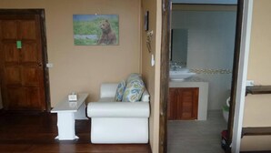 A room with a wooden floor, a white sofa with patterned cushions, a small white table, and a painting of a bear on the wall. - Rao Ga Khao Resort (Pak Chong)