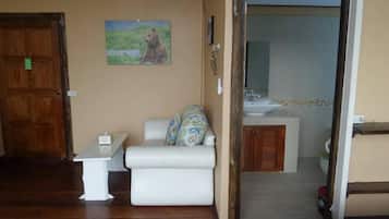 A room with a wooden floor, a white sofa with patterned cushions, a small white table, and a painting of a bear on the wall.