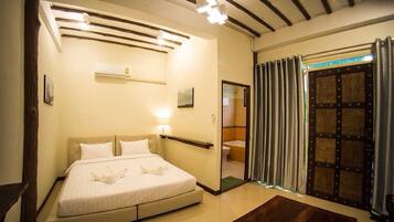 A hotel room with a bed, a bedside table, a mirror, a shower area, and a wooden floor.