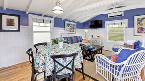 A dining area with a table set for four, surrounded by chairs. There is a sofa with cushions and a television mounted on the wall. - Best Beach Location in Santa Monica! Our Summer Stretches Through Fall! (Santa Monica)
