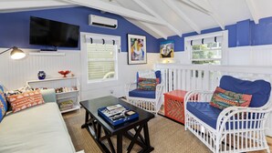 A room with a white ceiling, blue walls, a flat-screen TV, white wicker furniture, a small table with board games, and a window with blinds. - Best Beach Location in Santa Monica! Our Summer Stretches Through Fall! (Santa Monica)