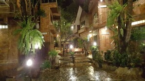A nighttime view of a courtyard with stone buildings, water features, and illuminated plants. - Treasure Inn Khaoyai (Pak Chong)